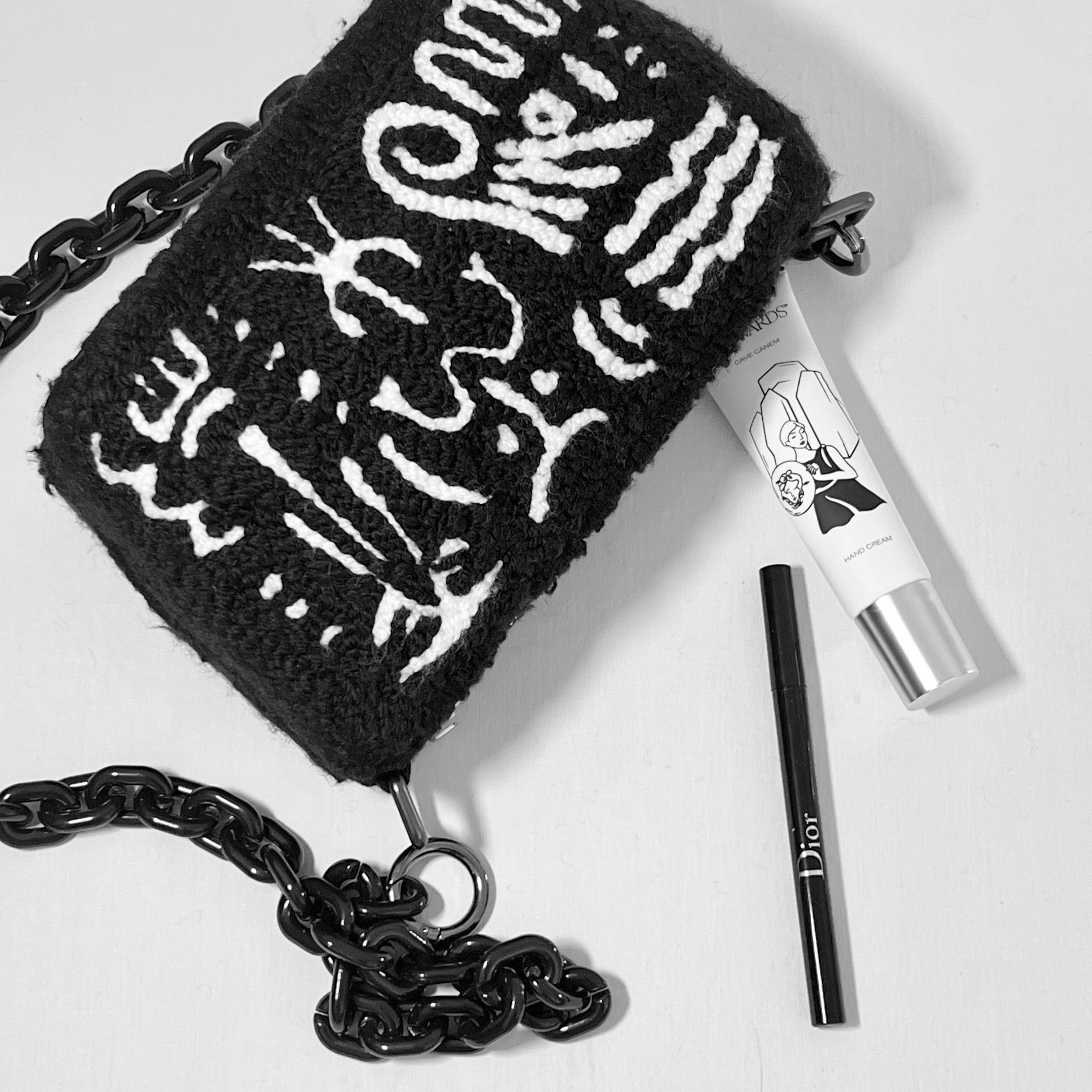 Flatlay of Ohpunch Pochette Water Cipher punch needle DIY bag with chain strap and essentials, showing capacity.